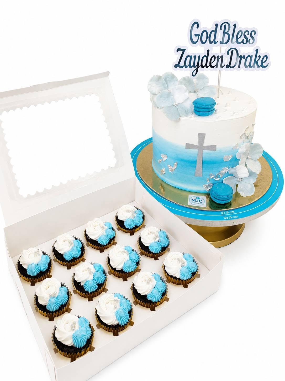 A white and blue christening cake with sugar flowers and a cross, reading God Bless Zayden Drake