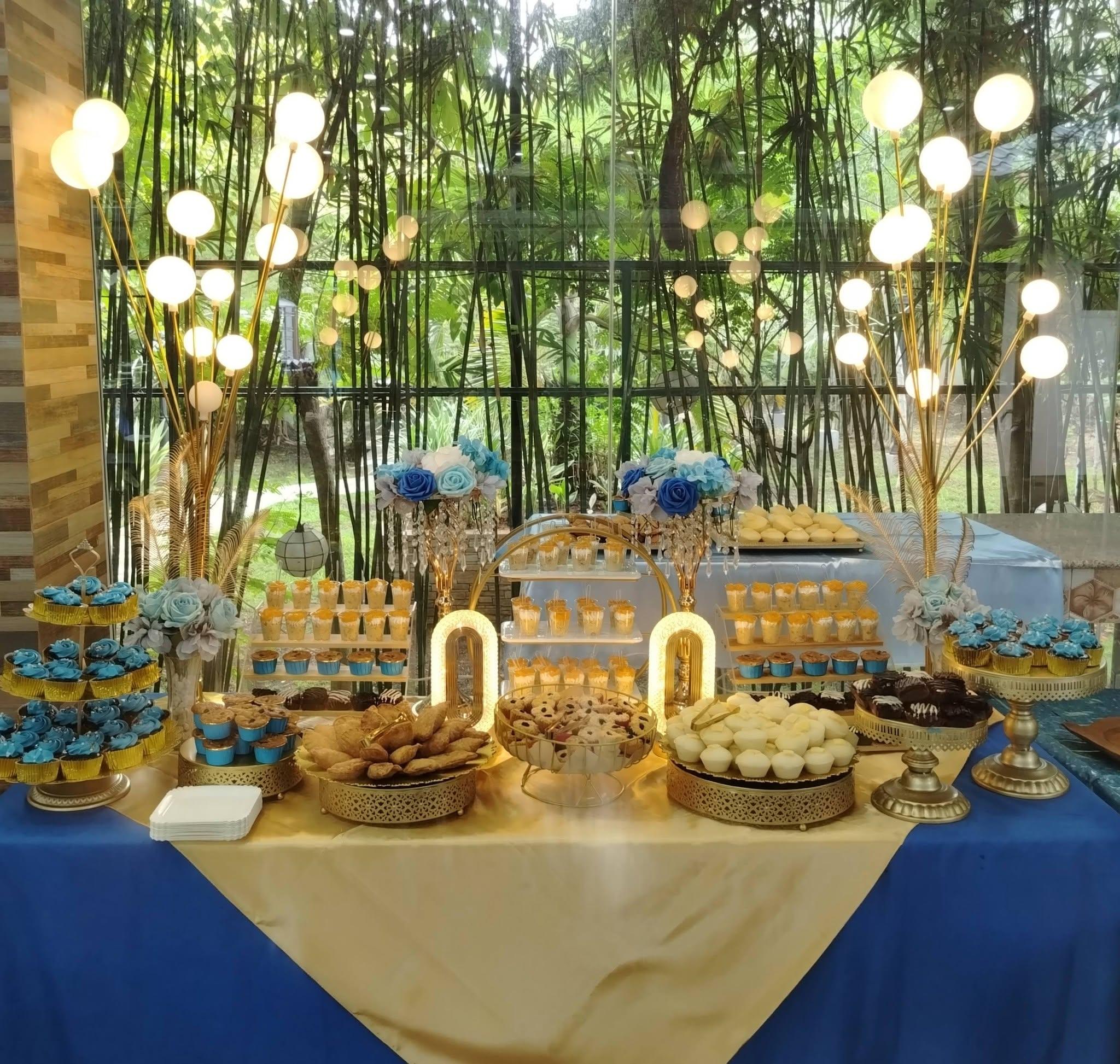 A dessert table of cupcakes, cookies, and pastries styled in blue and gold for an outdoor event