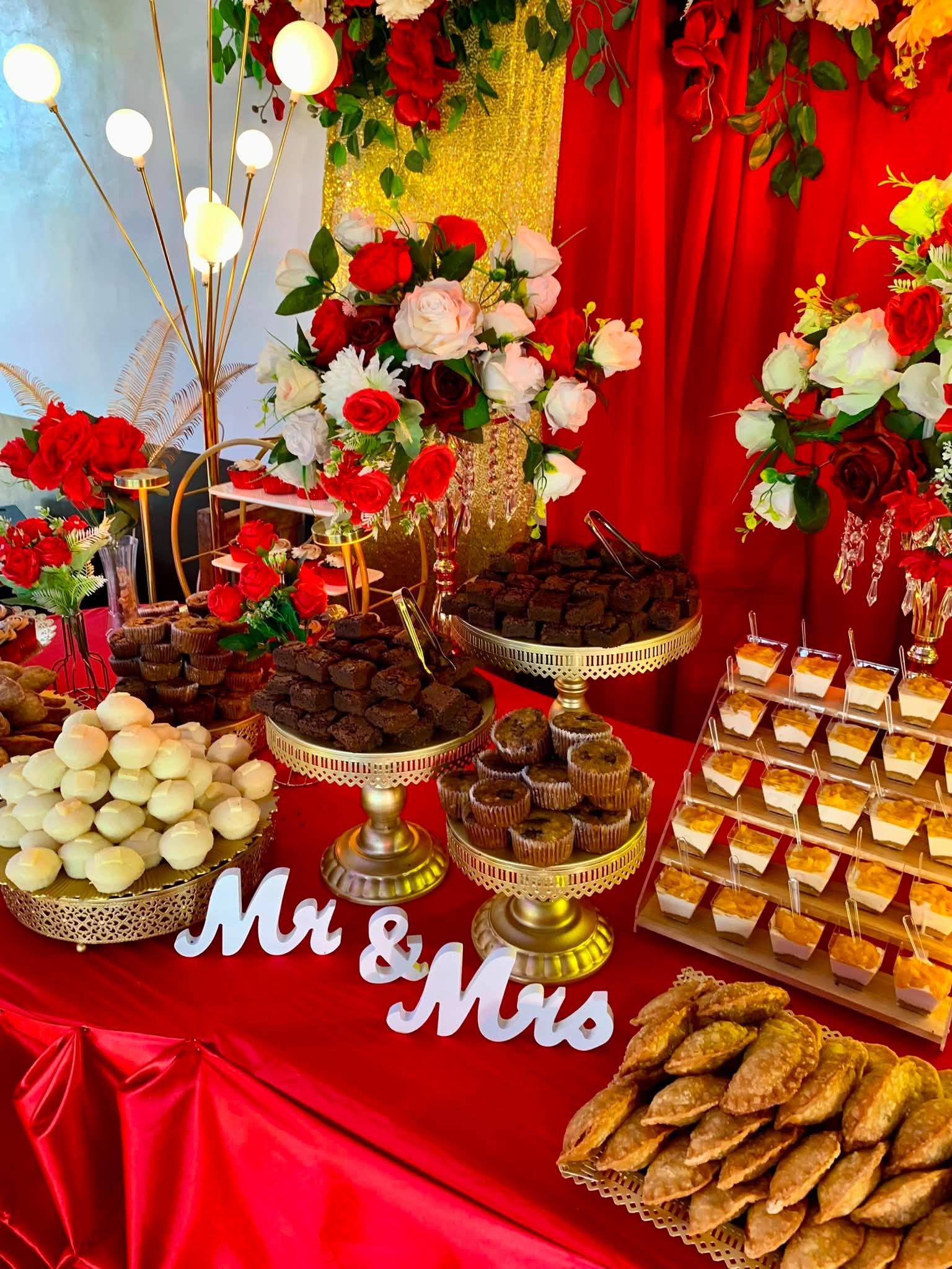 A styled dessert table in red and gold with a Mr and Mrs sign, brownies, cupcakes, and pastries for a wedding