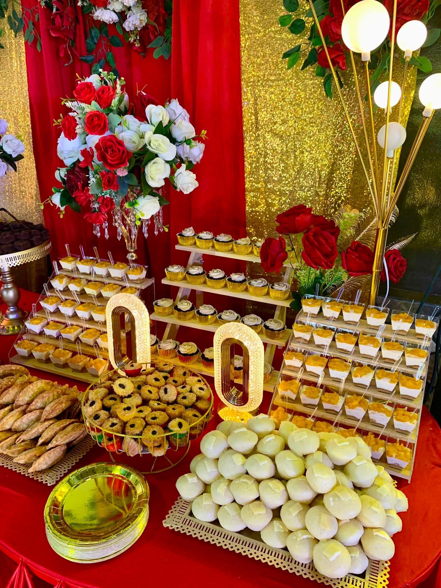 A red and gold dessert table with tiered cupcakes, mango float cups, empanada, and puto for a wedding reception