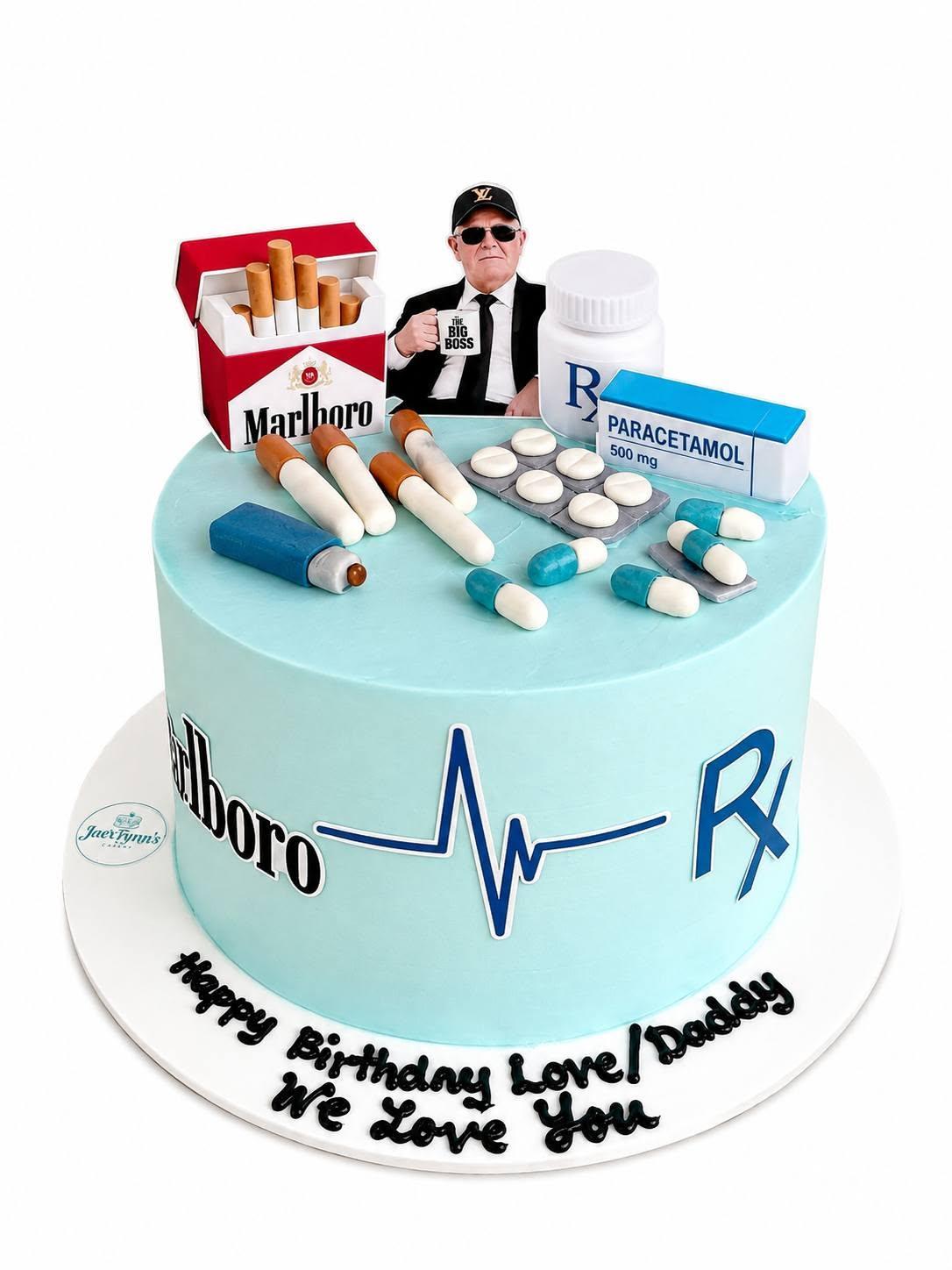 A pale teal cake decorated with a cigarette pack, pill bottles, and a heartbeat line as an inside joke
