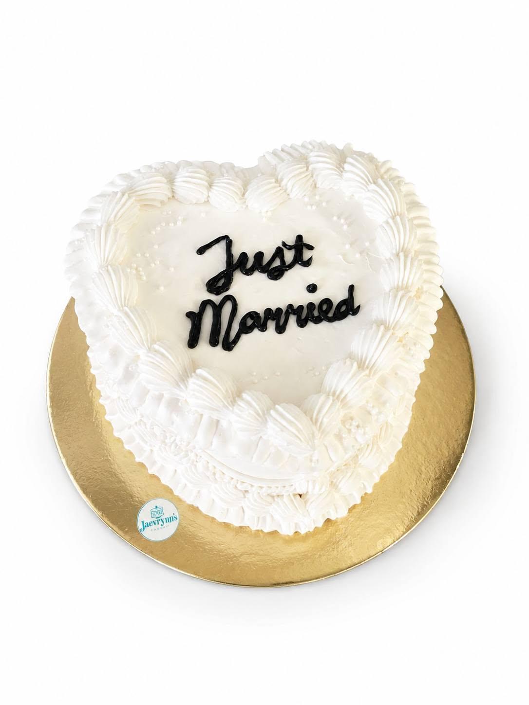 An all-white heart-shaped cake piped with shell borders, reading Just Married