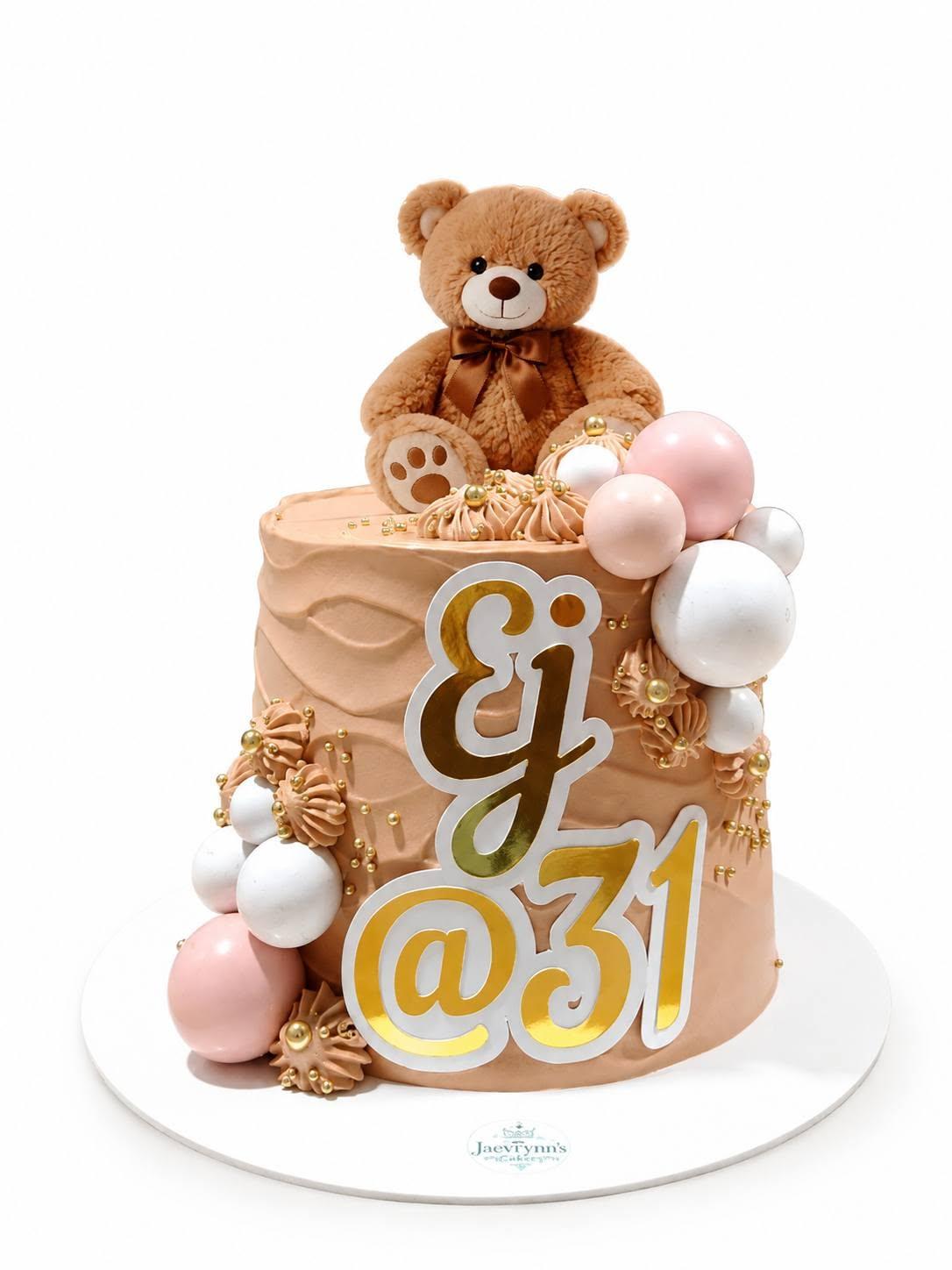 A tan-frosted cake with a plush teddy bear topper and pink and gold spheres, made for EJ's 31st birthday