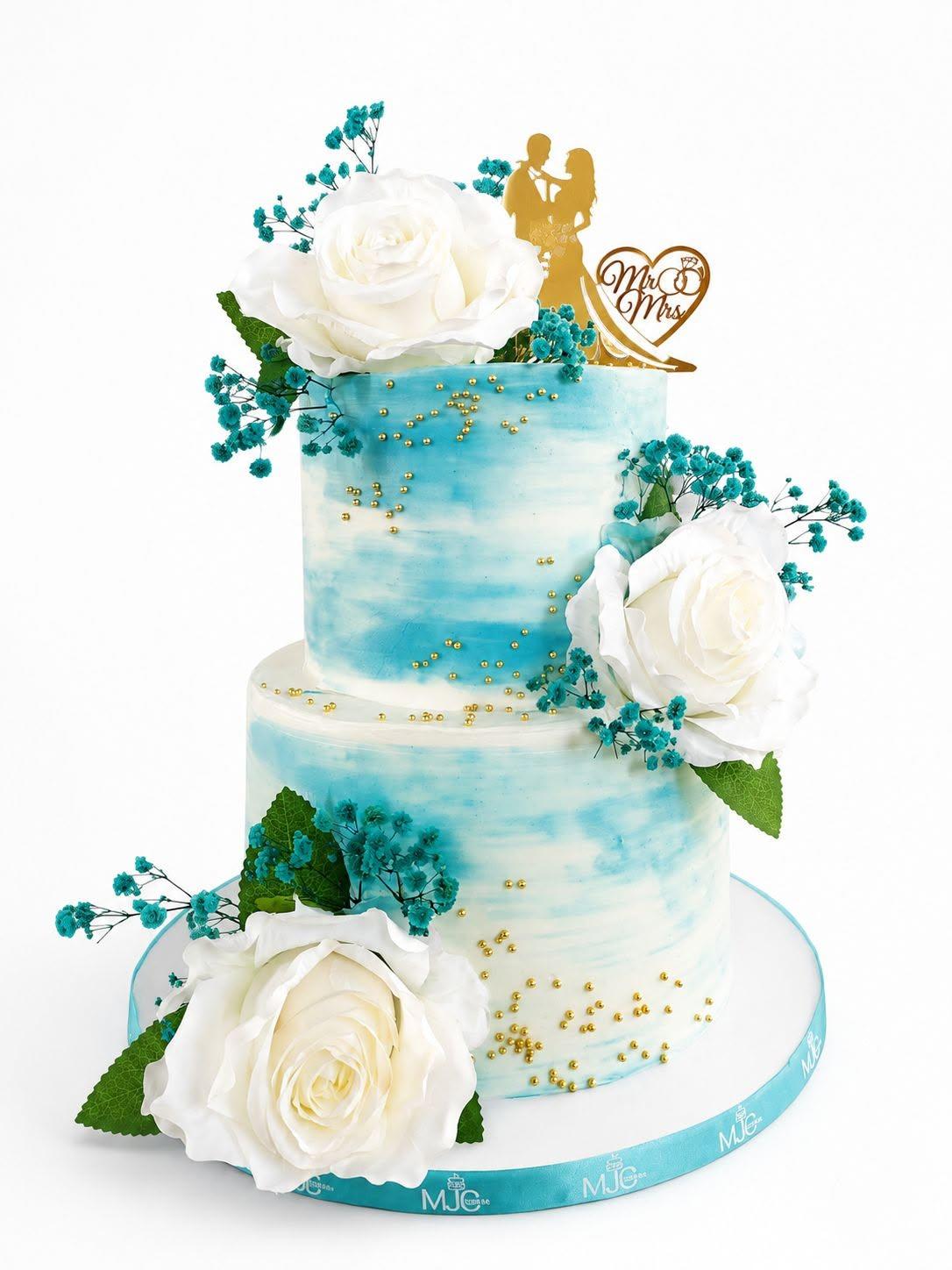 A two-tier teal and white watercolour wedding cake with sugar roses, gold pearls, and a Mr and Mrs topper